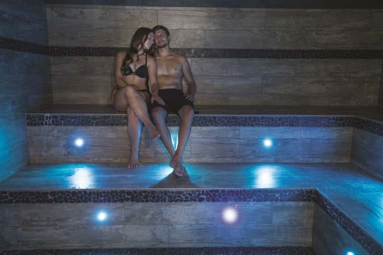 Spa hot tub with stone walls, blue underwater lighting, and two people relaxing