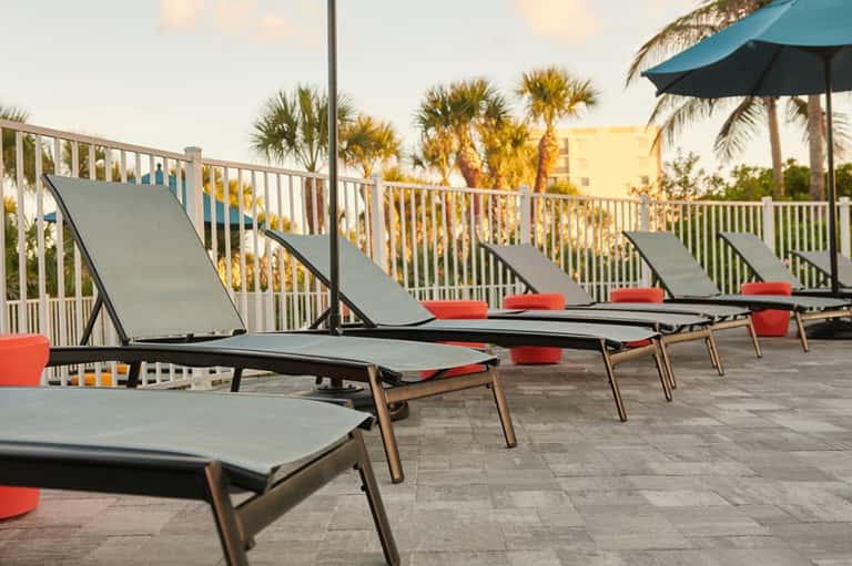 Beachfront deck with lounge chairs, red cushions, umbrellas, and palm tree views at golden hour