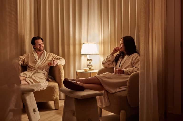Couple relaxing in spa robes in luxurious lounge with gold curtains and lamp