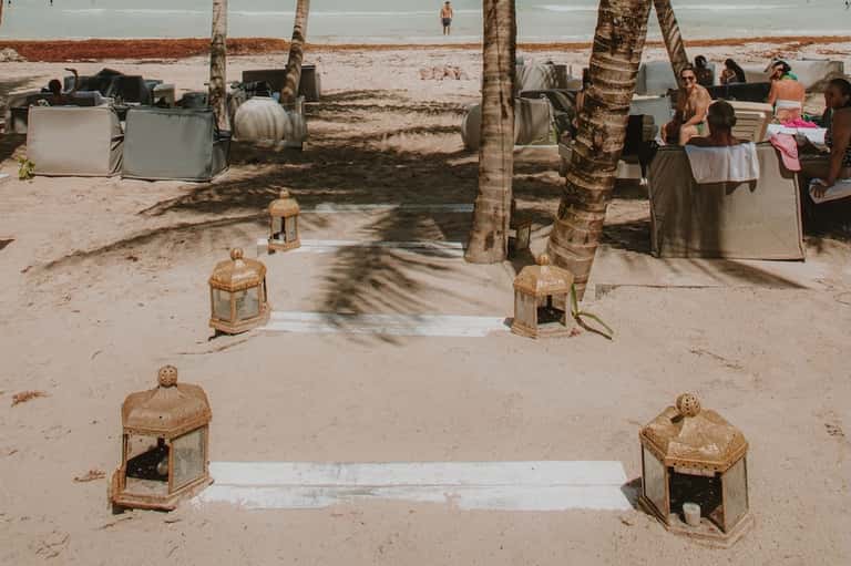Beach gathering with palm trees, seating areas, and people relaxing near shoreline