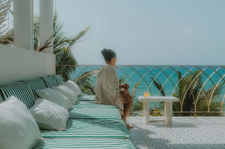 Woman relaxing on striped daybed on ocean-view terrace with palm trees and railing
