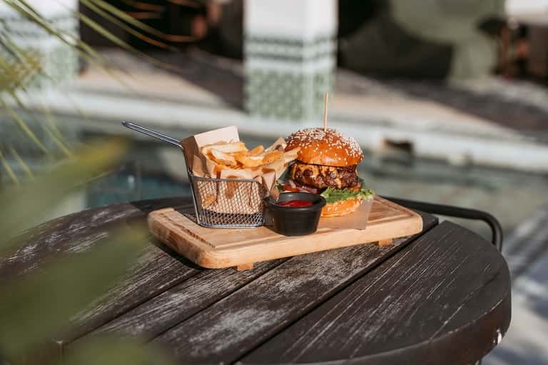 Gourmet burger with fries served on wooden board poolside with beverage