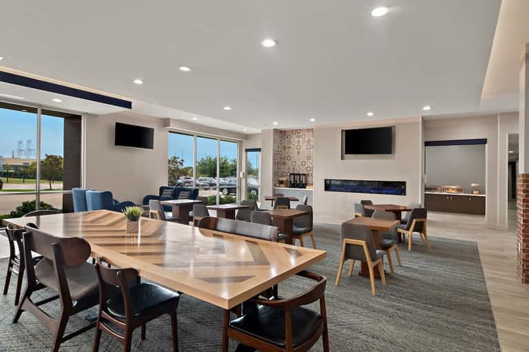 Modern hotel common area with wood tables, fireplace, large windows, and contemporary furnishings