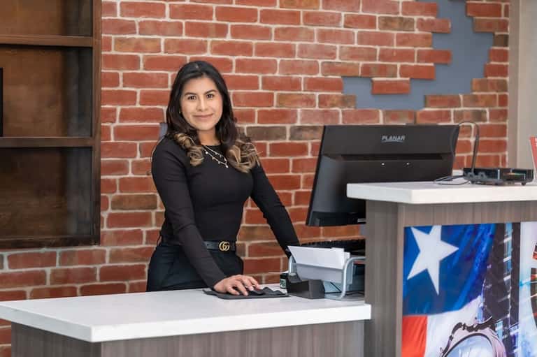 Professional woman at hotel front desk with brick wall backdrop and computer terminal