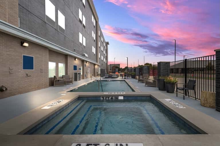 Outdoor lap pool and hot tub at hotel with modern brick building and purple sunset sky