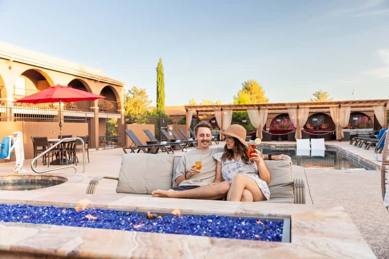 Couple relaxing in sunken lounge by resort pool with fire pit and covered dining area