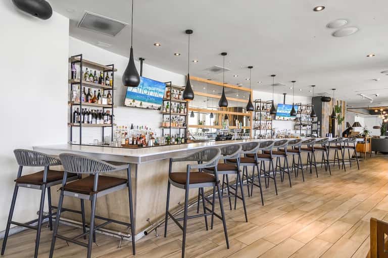 Modern hotel bar with white aesthetic, black pendant lights, and extensive bottle display