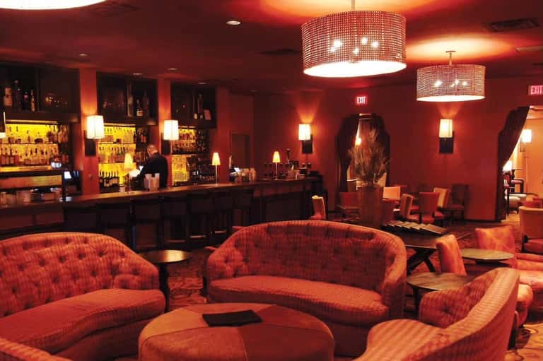Upscale hotel bar with red ambient lighting, curved seating, and illuminated liquor shelves