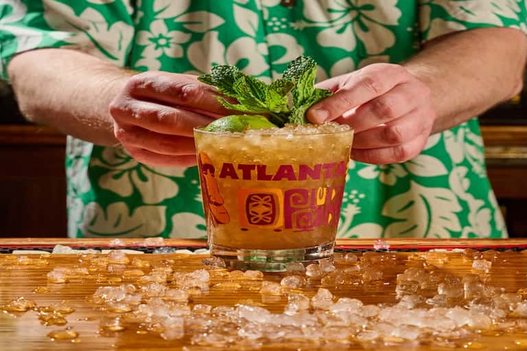 Tropical cocktail with mint garnish being served in branded glass with ice on wooden counter