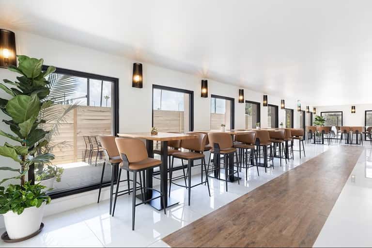 Modern hotel bar and lounge with high-top seating, extensive windows, and minimalist design