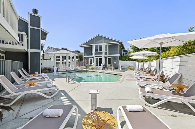 Residential pool area with modern homes, lounge chairs, umbrellas, and landscaping
