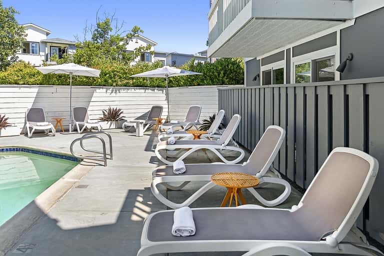 Residential pool area with white lounge chairs, umbrellas, white fence, and modern building