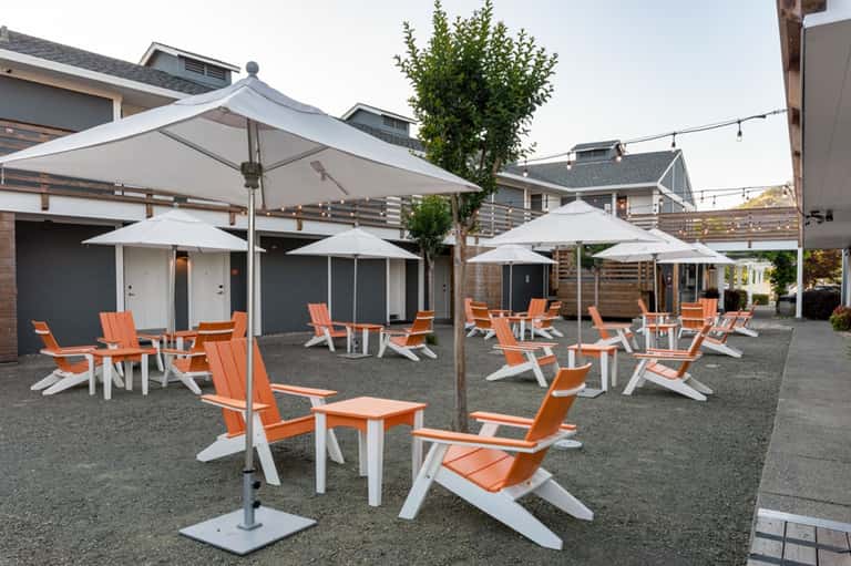 Outdoor patio with orange and white Adirondack chairs arranged under white umbrellas near residential homes