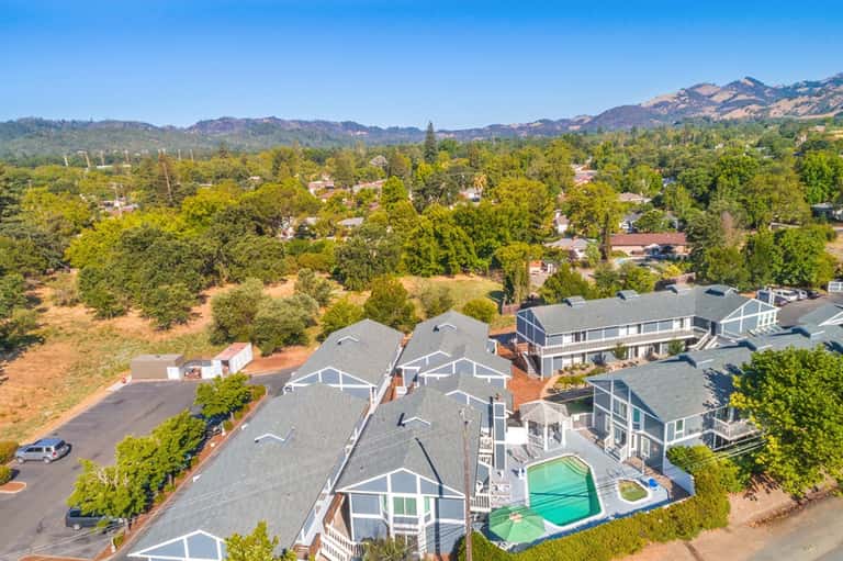 Aerial view of residential homes with swimming pool surrounded by trees and mountains in background