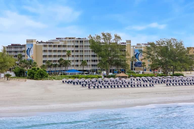 Beachfront hotel with multi-story tan building, blue and white striped umbrellas, and ocean view