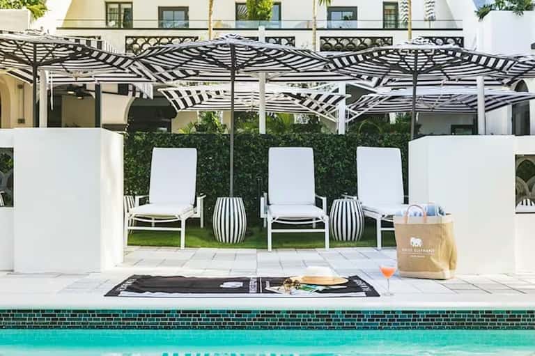 Luxury pool deck with lounge chairs, pergola shade structure, white privacy screens, and teal pool edge