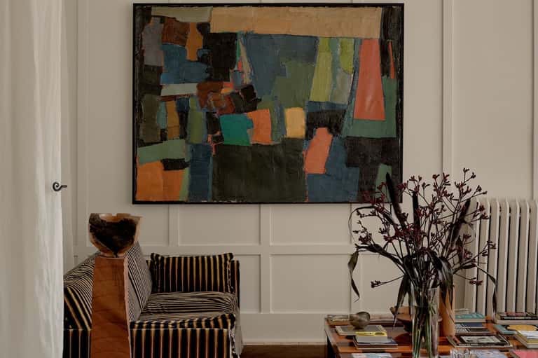 Living room with striped accent chair, abstract artwork, and botanical arrangement on side table