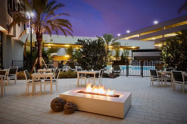 Elegant outdoor patio with fire pit, lounge seating, palm trees, and illuminated landscape at dusk