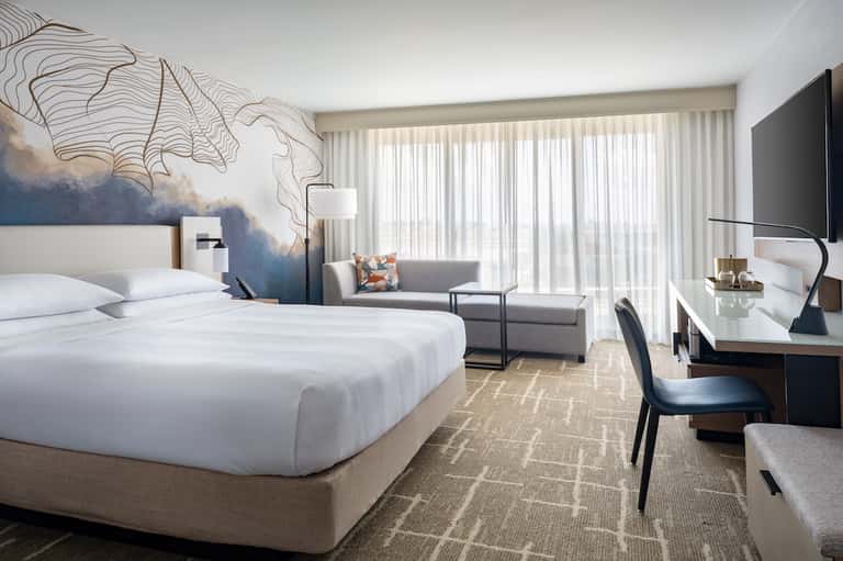 Luxury hotel room with king bed, modern artwork, seating area, and ocean-view balcony