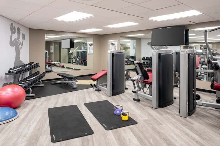 Fitness center with dumbbells, cardio equipment, exercise mats, stability balls, and mirrored walls