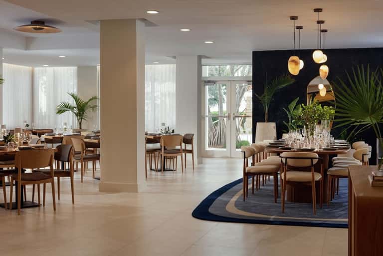 Contemporary dining room with wooden chairs, pendant lights, potted plants, and bright windows