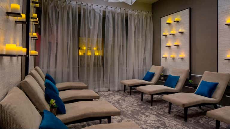 Modern spa lounge with beige loungers, blue pillows, and ambient candlelit wall