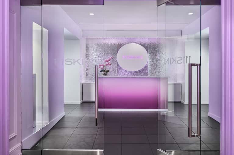 Minimalist pink neon spa reception with glass doors, white walls, and illuminated circular logo