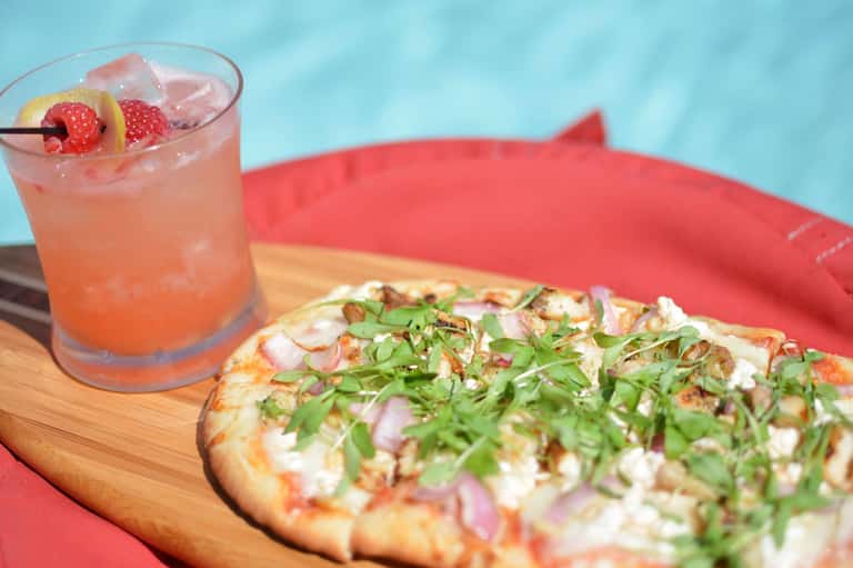 Refreshing cocktail with berries and a gourmet pizza with fresh herbs by the pool