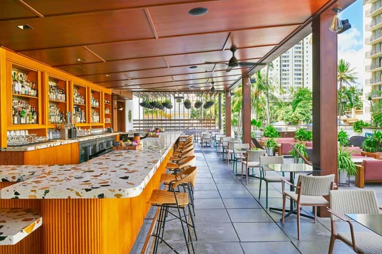 Open-air bar with wooden cabinetry, terrazzo counters, and tropical garden patio seating
