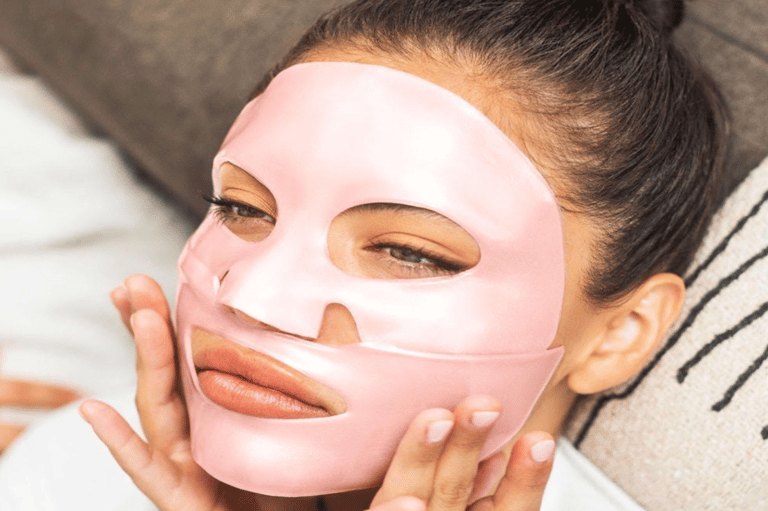 Woman applying pink sheet face mask for skincare treatment and relaxation