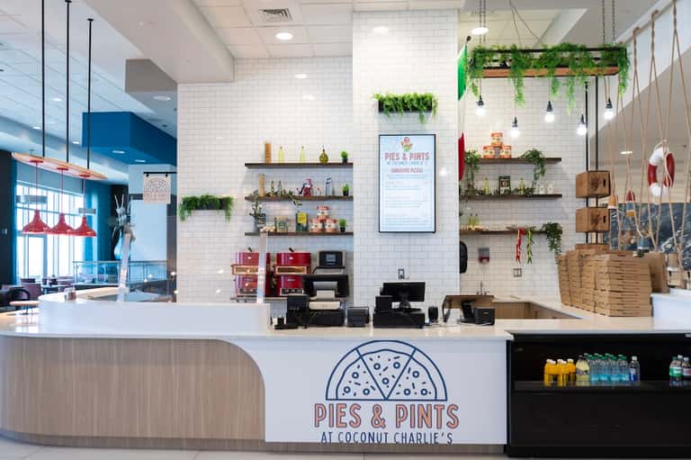 Bright café counter at Pies & Pints with white subway tile, floating shelves, and hanging plants