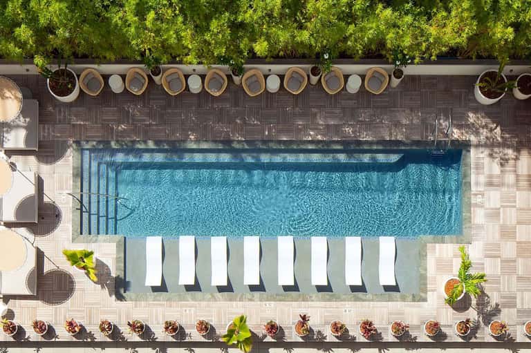 Aerial view of lap pool with lounge chairs, tropical landscaping, and woven shade structures along edge