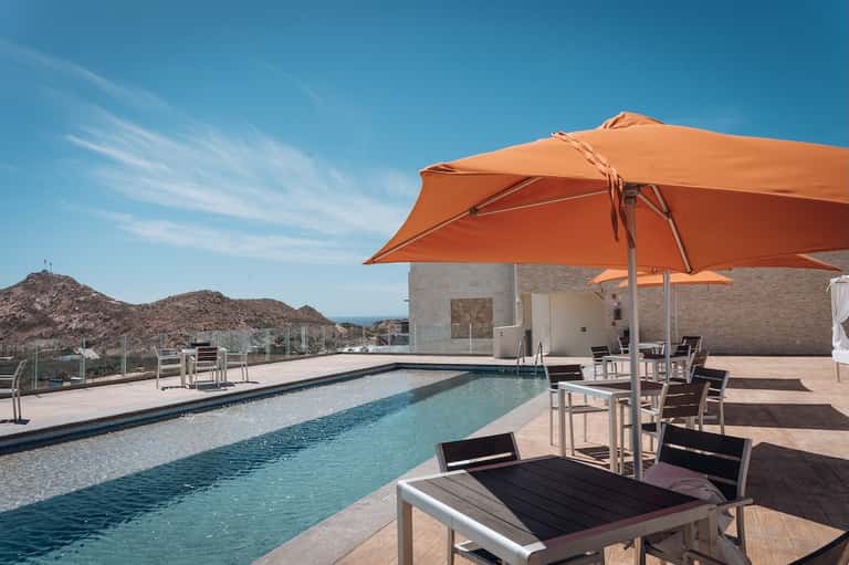 Rooftop pool with orange umbrellas, ocean view, desert mountains, modern architecture, and seating