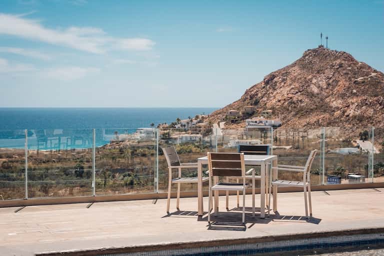 Beachfront terrace with dining table overlooking ocean, rocky coastline, and Mediterranean village