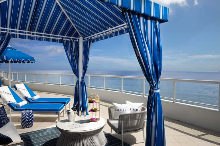 Oceanview balcony cabana with blue striped awning, lounge chairs, and water views