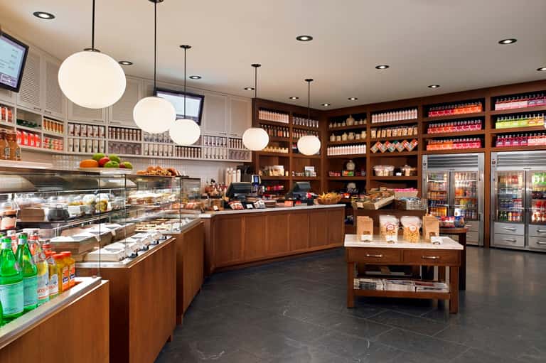Upscale café interior with wooden cabinetry, glass display cases, pendant lighting, and refrigerated units
