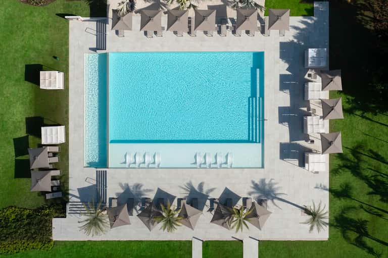 Aerial view of rectangular pool with surrounding lounge chairs and dark umbrellas on concrete patio