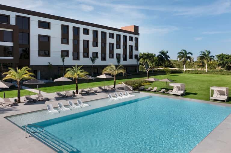 Contemporary resort pool with white loungers, manicured lawn, and modern white building