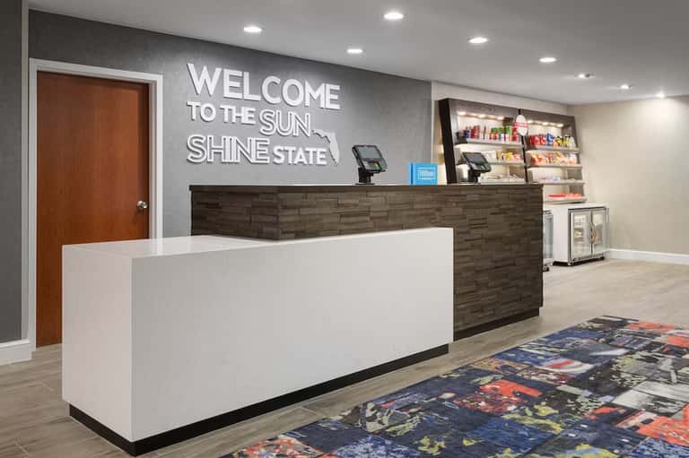 Hotel lobby reception desk with 'Welcome to the Sunshine State' sign and merchandise shelving