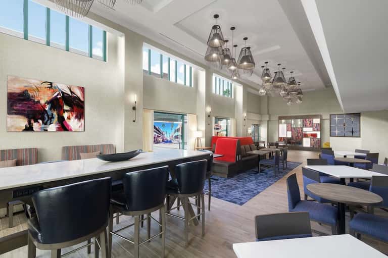 Modern hotel lobby with high ceilings, pendant lights, dining area, and lounge seating
