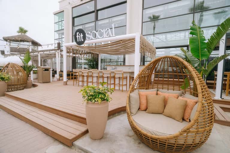 Modern beachfront social lounge with woven egg chairs, palm plants, and casual dining area