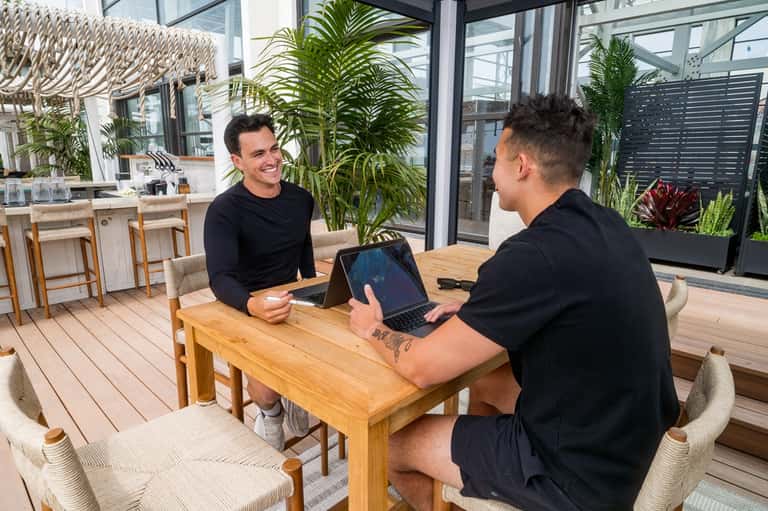 Two men conducting business meeting on tropical deck with plants and lounge seating