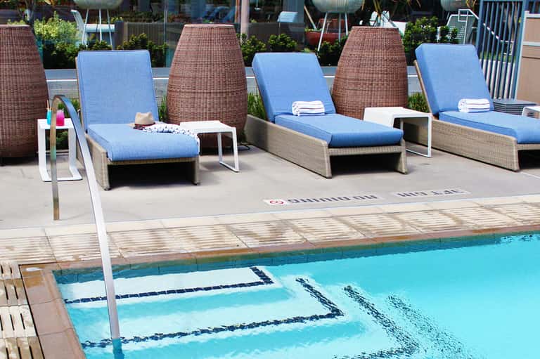 Resort pool deck with blue lounge chairs, wicker privacy screens, and clear turquoise swimming pool