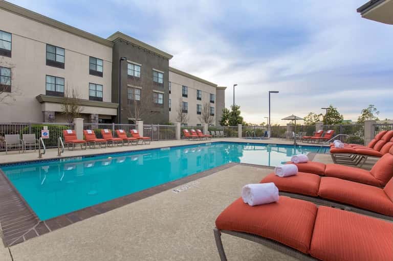 Resort swimming pool with bright blue water, red loungers, hotel building, and manicured grounds