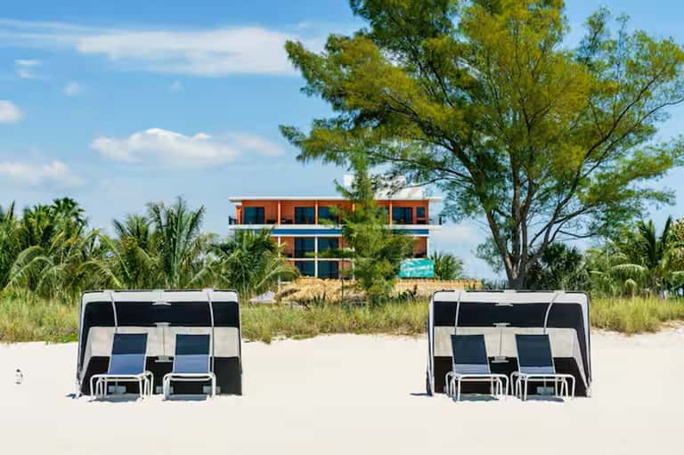 Modern beachfront resort building with orange and blue facade, palm trees, and beach cabanas