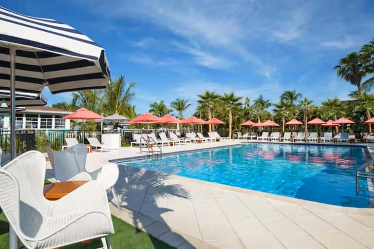 Resort pool with red umbrellas, lounge chairs, and tropical palm trees