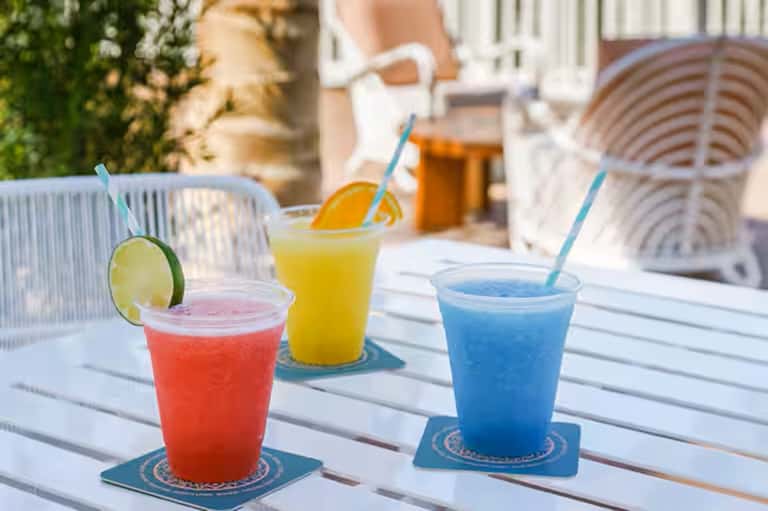 Three colorful cocktails on white table with wicker chairs in outdoor patio setting