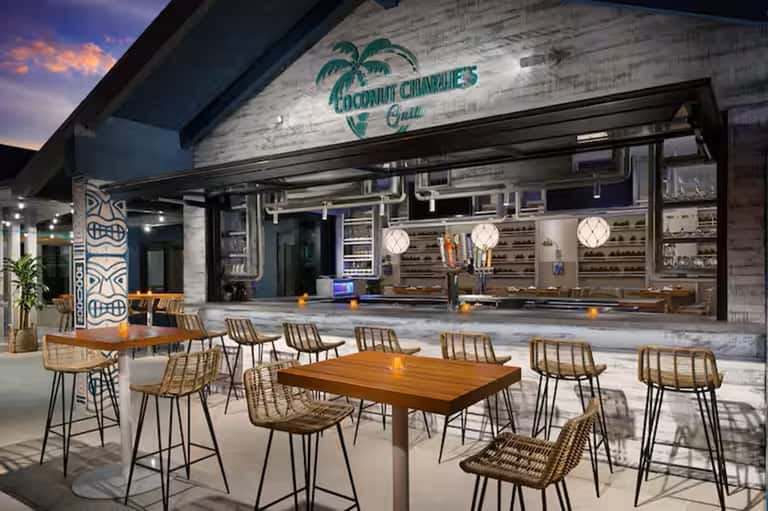 Modern outdoor tiki bar with white weathered wood signage, woven bar stools, and open kitchen design