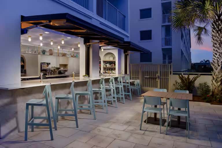 Contemporary outdoor bar area with blue-green seating, modern bar counter, and palm trees at dusk