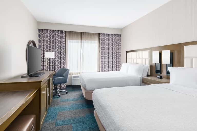 Hotel double queen bedroom with patterned curtains, flat-screen TV, and bathroom vanity
